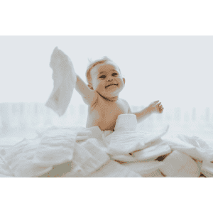 Baby smiling and playing with diapers in a bright, cheerful nursery setting, representing essential baby products delivery in Stamford for parents and caregivers.