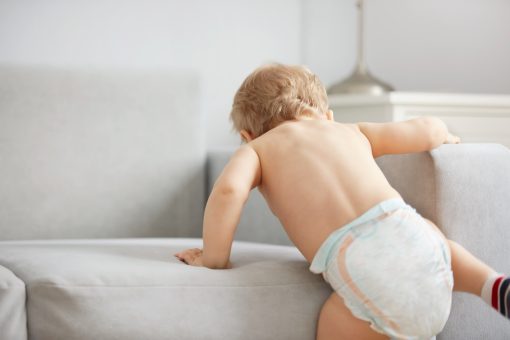 Baby boy climbing onto a sofa in a modern living room for baby essentials delivery.