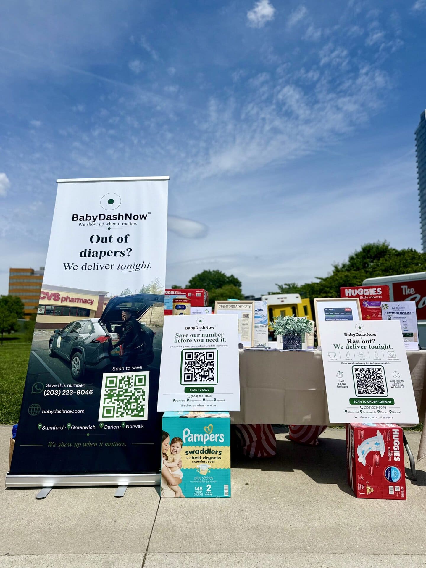 BabyDashNow booth at Stamford Day 2026 with banners, QR codes and diaper packs on display